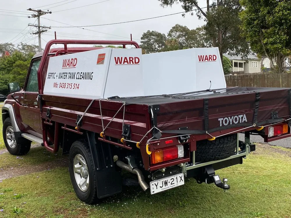 The maroon Ward ute, signwritten Ward Septic and Water Tank Cleaning, parked on the grass verge