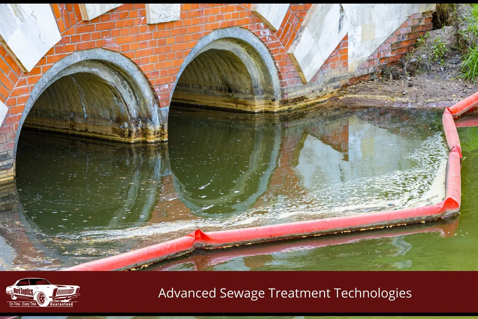 A bright red containment boom floats in dark water in front of two large concrete culverts beneath a brick arch bridge structure.