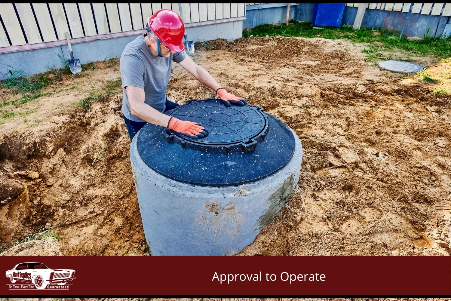 A worker in a red hard hat and orange gloves secures a black lid onto a concrete septic tank riser in a dirt-filled yard