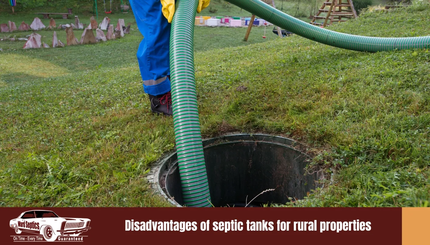 A worker in blue overalls and yellow gloves lowering a large green vacuum hose into an open circular septic tank riser on a grassy lawn.
