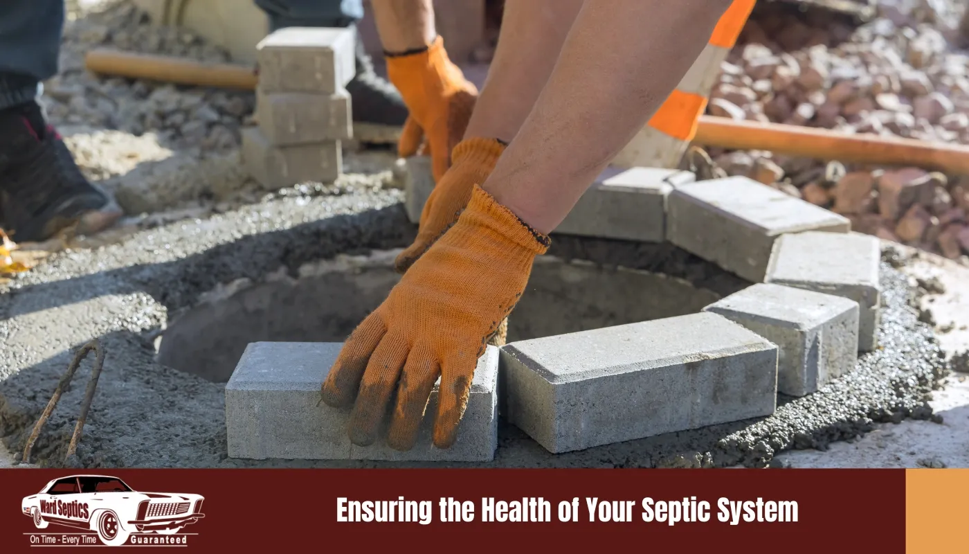 A worker wearing orange gloves laying concrete bricks in a circular pattern around an open manhole on a layer of fresh wet mortar.