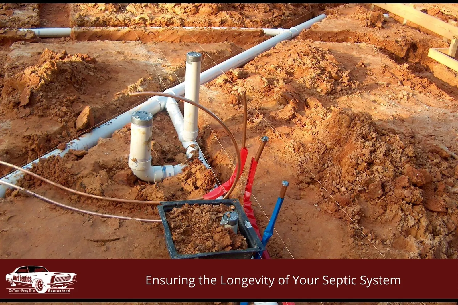 White PVC plumbing pipes and copper lines are laid out in a red dirt excavation for a building foundation.