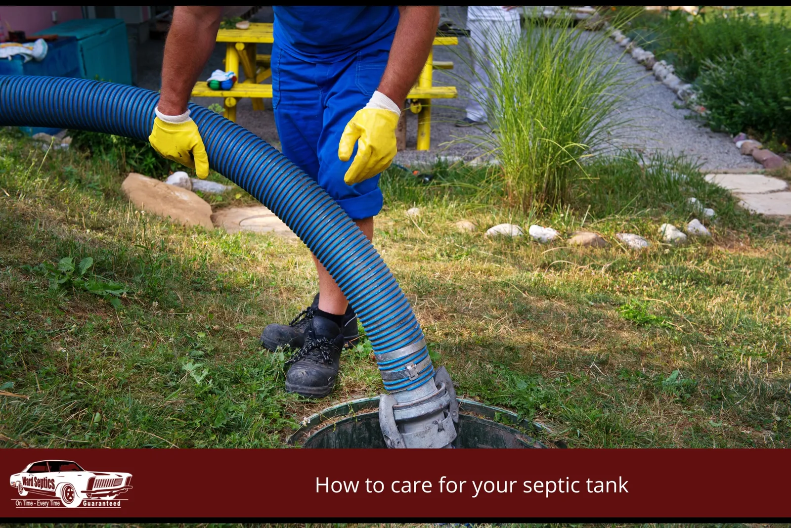 A worker in blue workwear and yellow gloves guiding a large blue suction hose into an open ground-level septic tank hole.