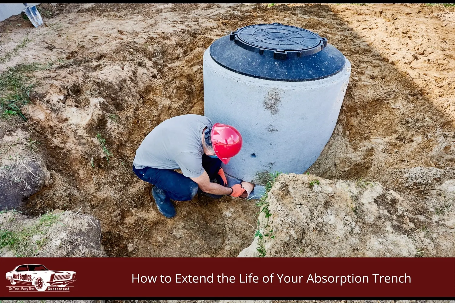 A red hard hat crouches down to connect a low-level pipe to a large cylindrical concrete pump well tank installed in a dirt pit.