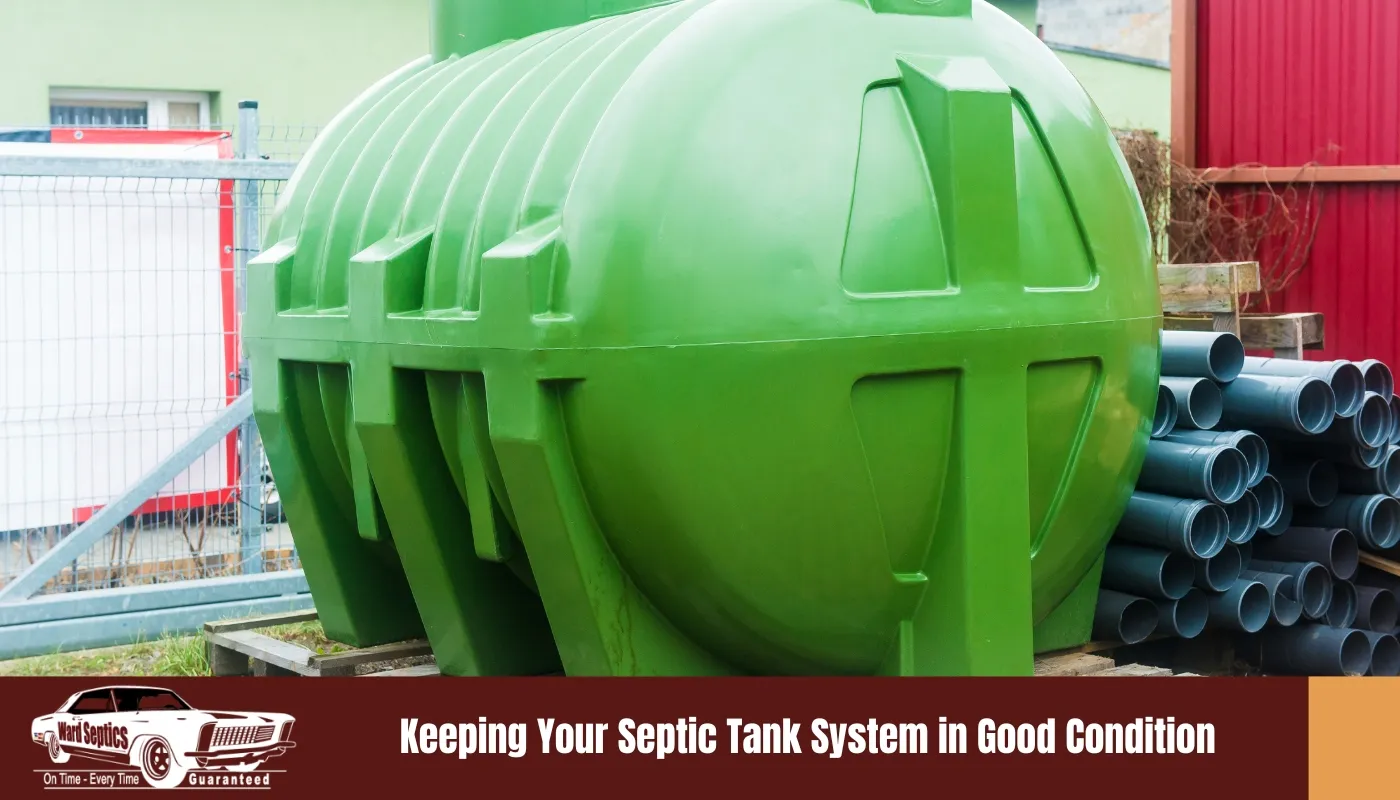 A large green plastic septic tank sitting on wooden pallets next to a stack of grey PVC pipes