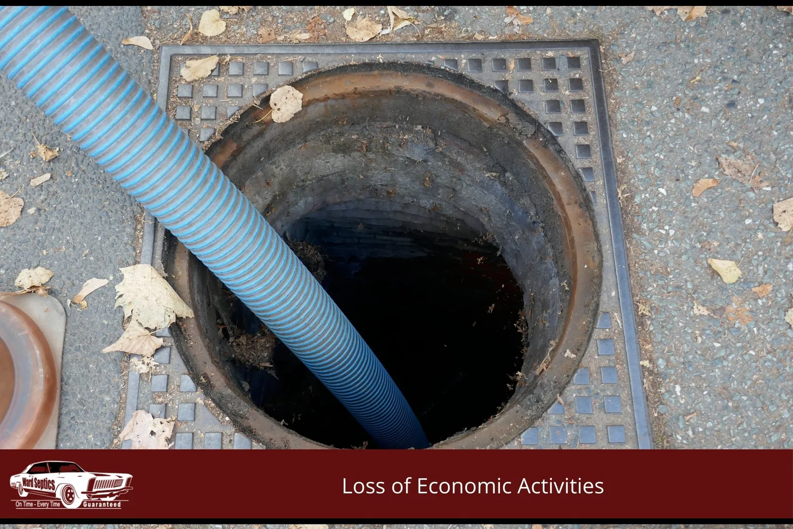 A blue corrugated suction hose extends into an open, dark manhole set in a paved surface.