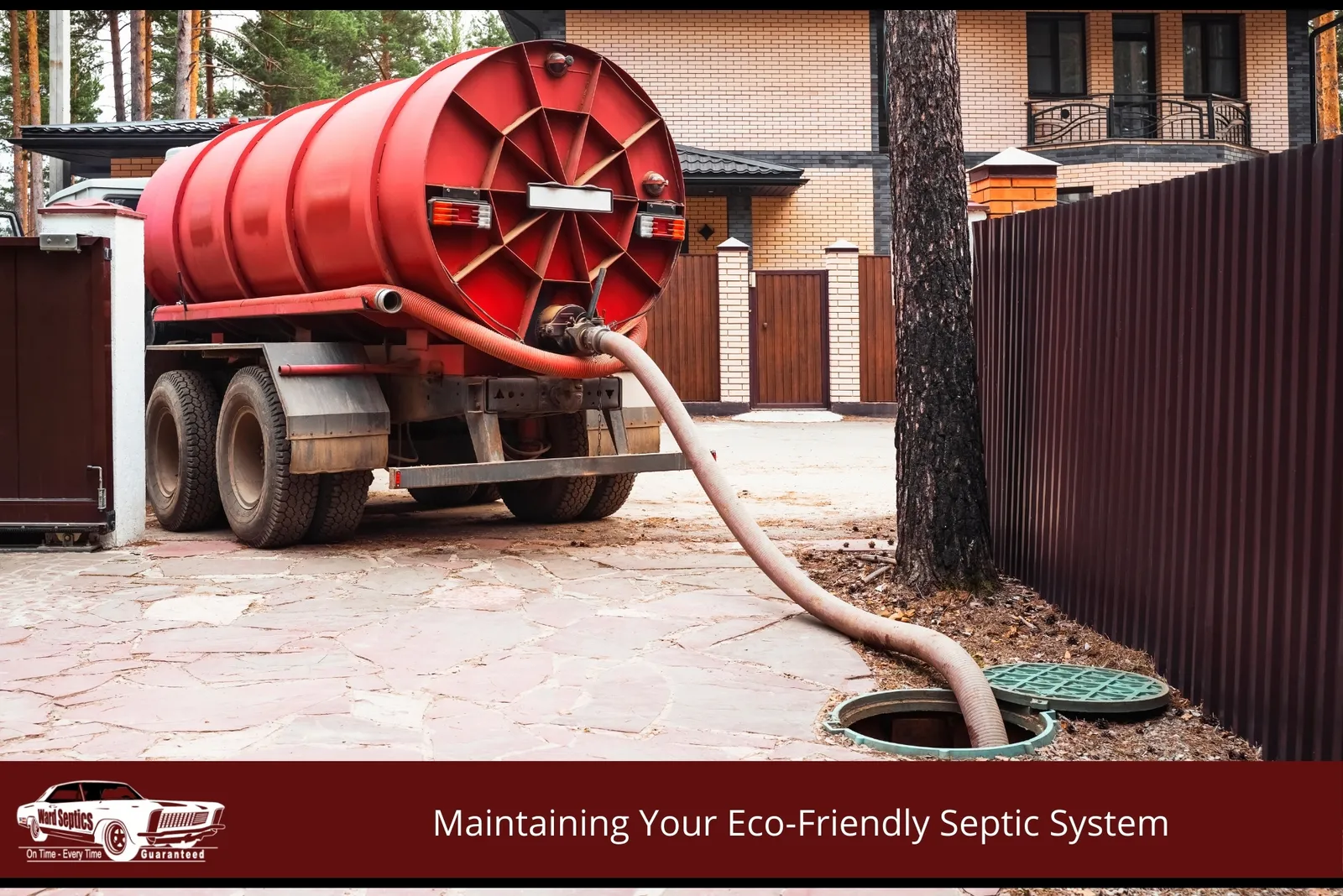 A red vacuum truck is parked on a stone driveway, with its large suction hose extended into an open septic tank manhole.