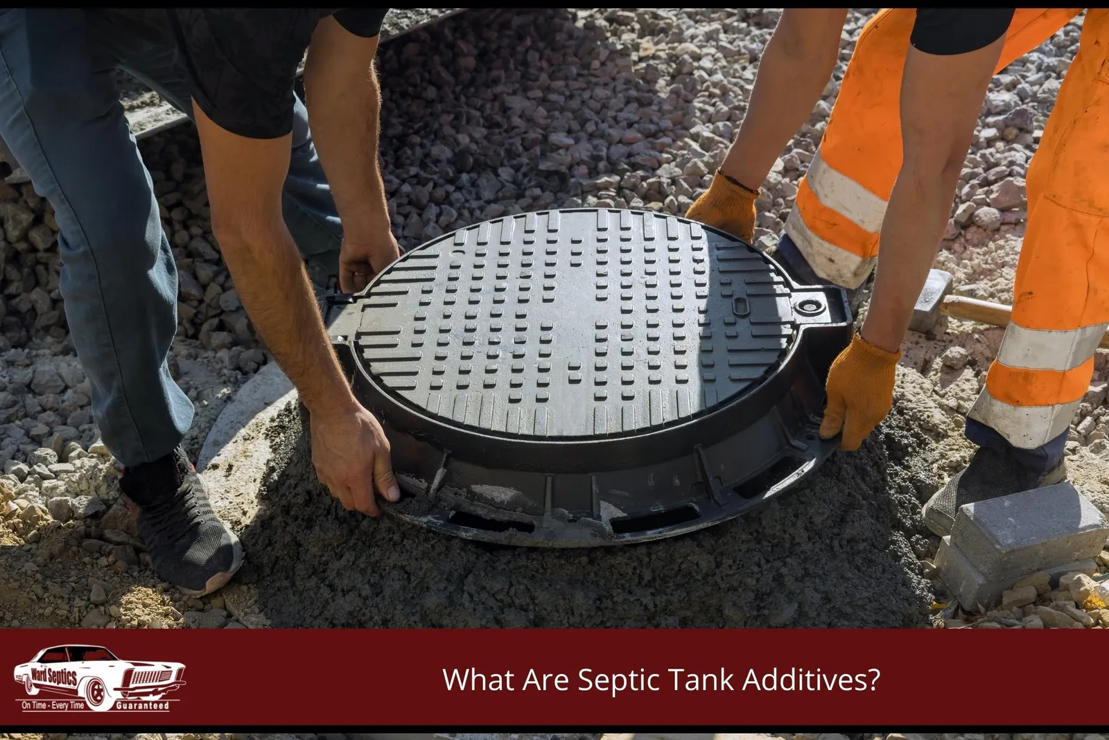 Two workers installing a heavy, ribbed black manhole cover onto a freshly laid concrete ring base on a gravel surface.