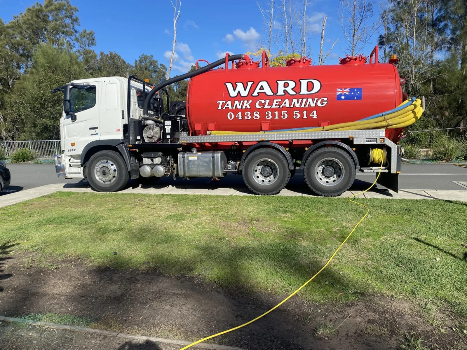 The red Ward Tank Cleaning truck parked on the street edge of a Central Coast property