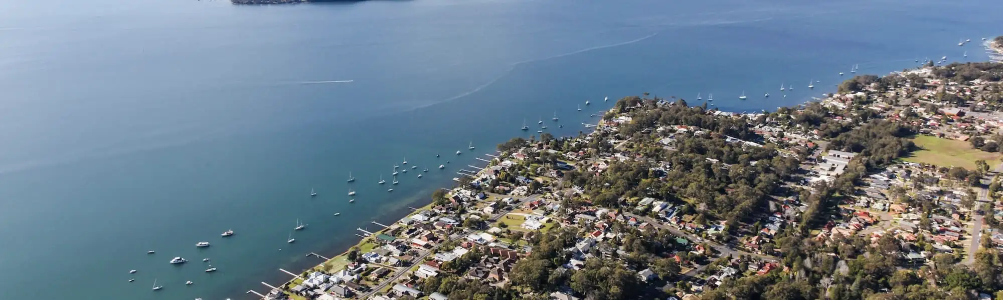 Aerial view of Lake Macquarie's shoreline, moored boats and lakeside homes backing onto bushland