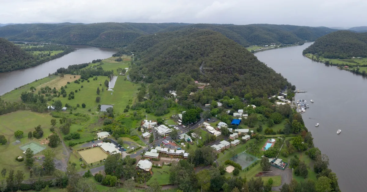 Aerial view of Wisemans Ferry village on its bend of the Hawkesbury River, bushland ridges behind