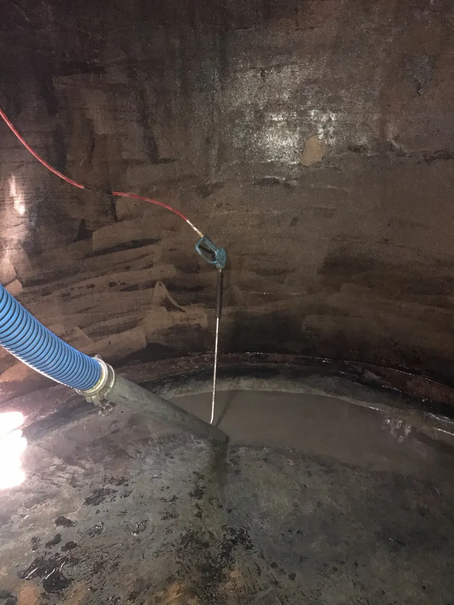 Inside a concrete water tank mid-clean, the pressure lance working over the walls and the suction hose drawing sludge from the base